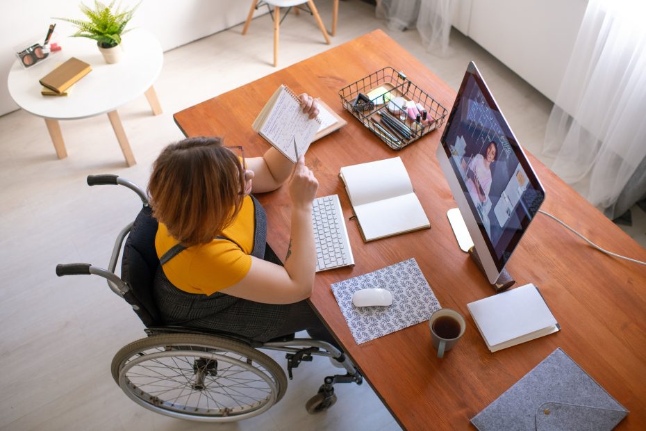 Woman in wheelchair participates in an online event while taking notes.
